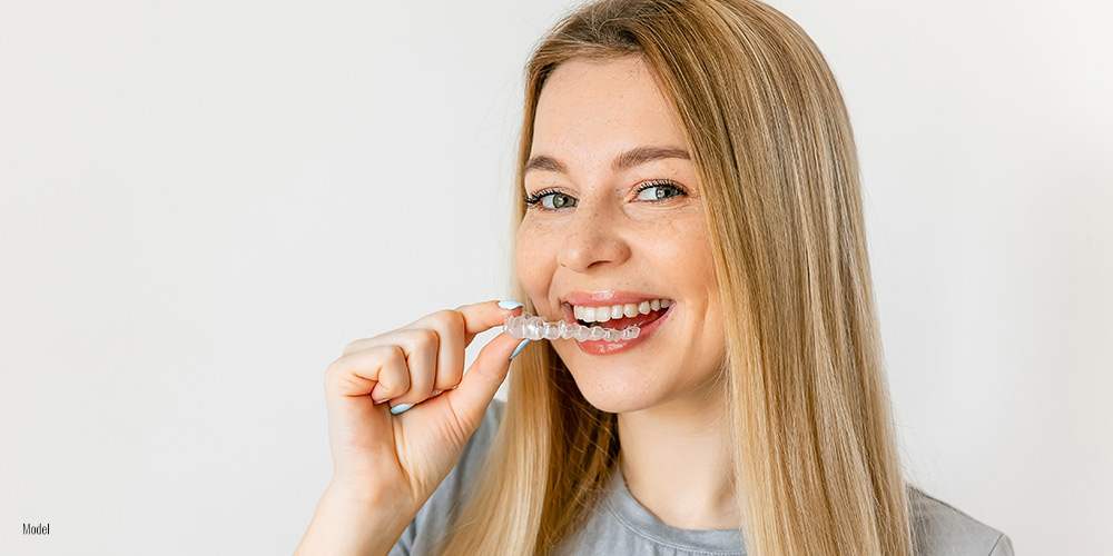 Girl smiling and holding Invisalign® in her hand