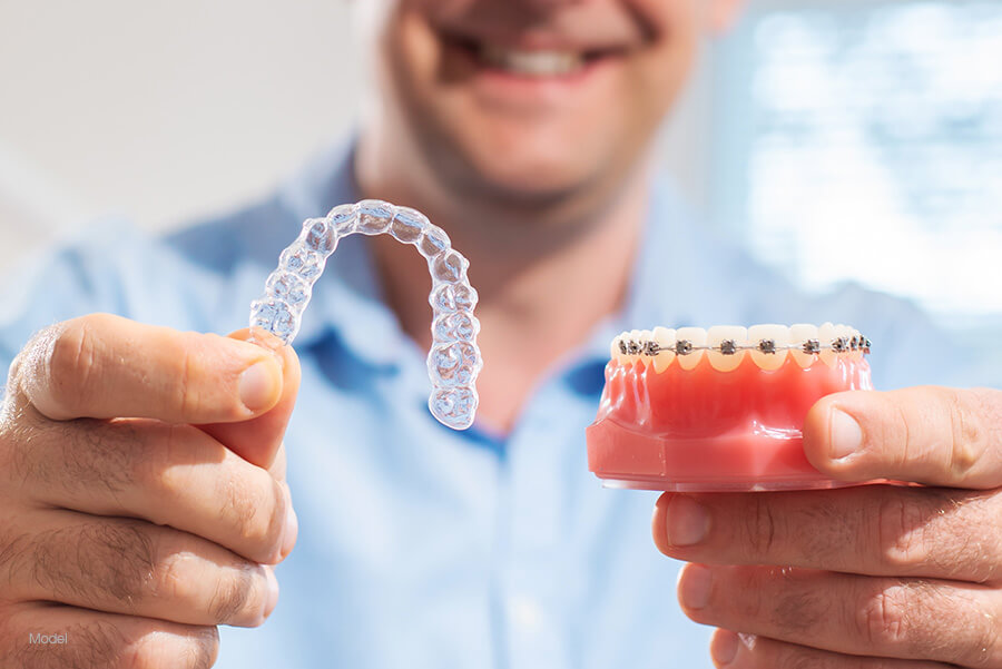 Man holding an Invisalign® aligner and a model of traditional braces.